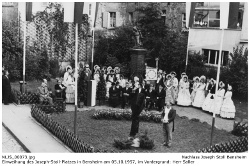 Einweihung des Josef Stoll-Platzes am 5. Oktober 1957. Blick auf die noch verhüllte Holzsäule. Daneben Herr Saller, im Hintergrund links: Vertreter der Stadt Bensheim, hinter der Säule Familie Stoll, Stoll-Berberich, stehend dahinter die Biedermeiergruppe der Heimatvereinigung Oald Bensem.; Kennung: NLJS_00073