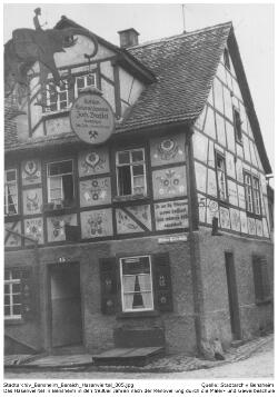 Bensheimer Hasenviertel, Das Ergebnis der Verschönerungsarbeiten durch die Maler- und Gewerbeschule, Aufschrift Schild: Kohlen; Kolonialwaren; Joh. Brestel; Nachfolger; Inh. Joh. u. Lorenz Brestel. Aufschrift an der Hauswand (Hintergrund): Is an de Stiwwel woas bassiert, hier wärrnse billig reperiert. Quelle: Stadtarchiv Bensheim.