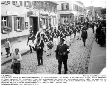 NLJS00022.jpg; Nachlass Joseph Stoll, Bensheim; Erster offizieller Auftritt der Bensheimer Bürgerwehr der Heimatvereinigung "Oald Bensem" in Weinheim am 05.07.1931, Bereich Hauptstraße 162 (heute: Hauptstraße 3). Im Hintergrund "Fitzers Bier- und Weinstube", im Vordergrund "Tapeziermeister Nikolaus Müller". Die Bürgerwehr wird angeführt durch den Vereinsgründer Joseph Stoll (1879 - 1956); Stempel auf Rückseite des Bildes: Bahnhof-Hotel & Restaurant, Weinheim a.d. Bergstrasse, Bes. Karl Bachmaier, Bleistiftvermerk: 1931, Größe des Fotos: 7,9 cm x 5,5 cm; digitalisiert und zusammengestellt: Frank-Egon Stoll-Berberich, 2023.